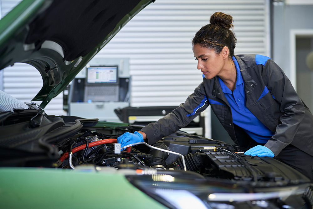 Technicienne en gants bleus travaillant sur le moteur d'une voiture Ford verte capot ouvert.