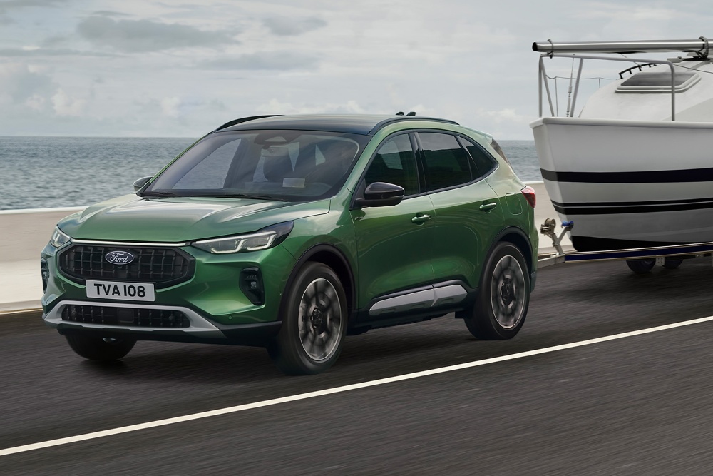 Ford Kuga verte tractant un petit bateau le long d’une route côtière.