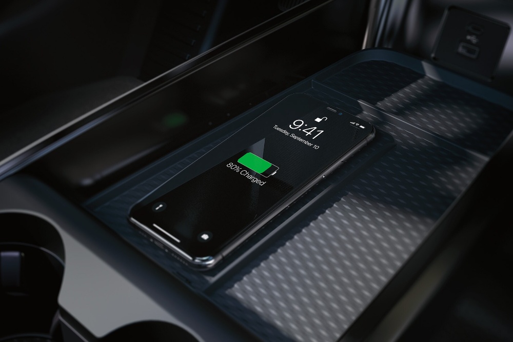 Gros plan du socle de recharge sans fil dans la console centrale, avec un iPhone en cours de chargement.