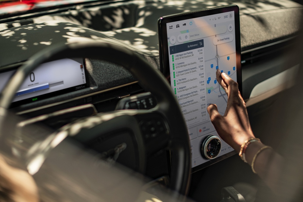 Gros plan d’une femme assise dans une Ford Mustang Mach-E, interagissant avec le grand écran tactile SYNC.