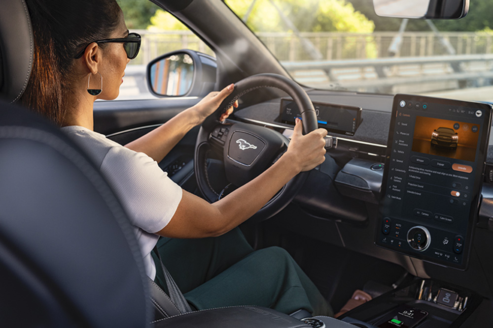 Une femme conduisant la Mustang Mach-E avec ses mains sur le volant. L’écran tactile de 15,5" indiquant des informations sur la voiture.