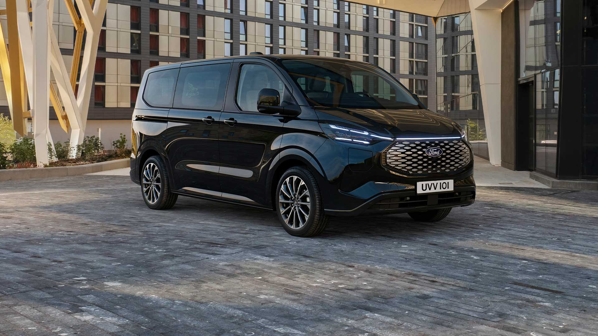 Un Ford E-Tourneo Custom noir est stationné devant un bâtiment moderne.