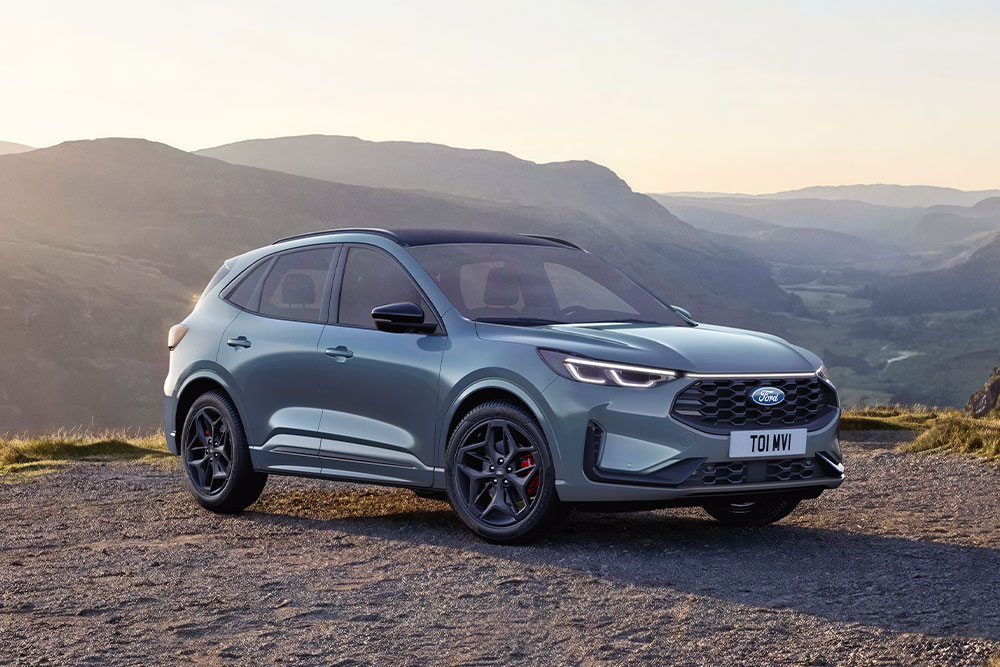 Un Ford Kuga gris garé sur une route de montagne en gravier au coucher du soleil.