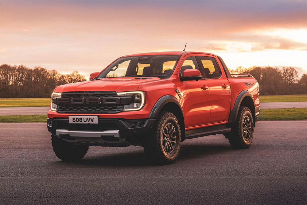 Un pick-up Ford Ranger Raptor orange stationné dans un paysage pittoresque.