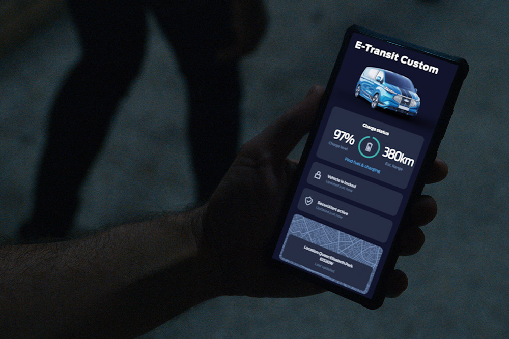 Un smartphone affichant un E-Transit Custom dans l’App Ford, indiquant le niveau de charge du véhicule et son emplacement.