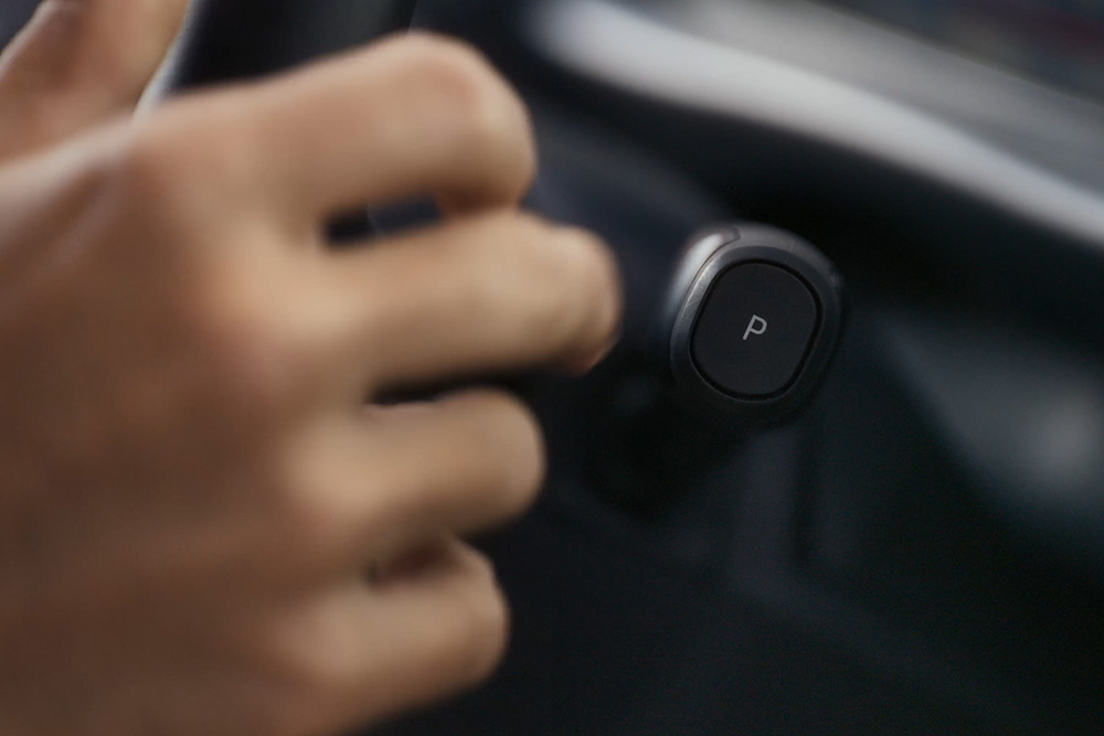 A hand is shown engaging the "P" (Park) button on the gear selector of the Ford Tourneo Custom.