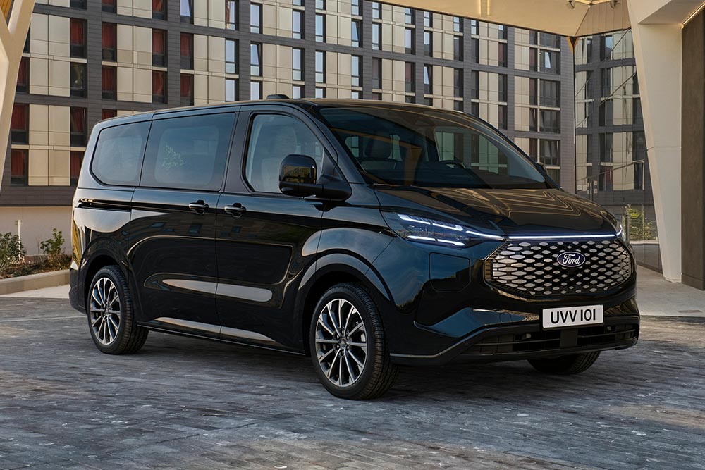 Un Ford E-Tourneo Custom noir est stationné devant un bâtiment moderne.