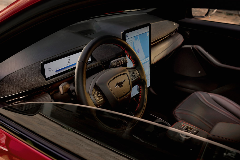 Intérieur d'un Ford Mustang Mach-E, montrant le volant, le tableau de bord numérique et le grand écran tactile central.