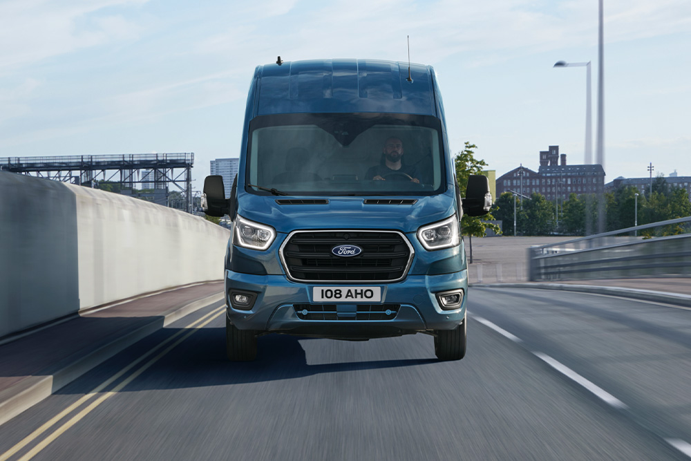 Vue de face d’un fourgon Ford Transit bleu circulant sur une route.