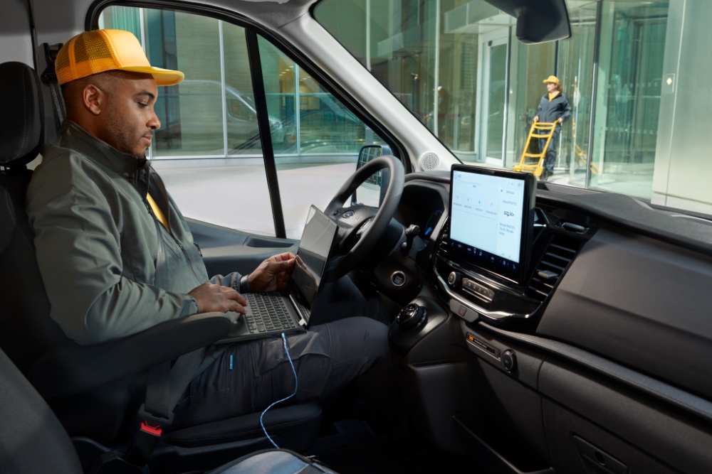 Un homme assis sur le siège du conducteur d’un fourgon Ford Transit, utilisant un ordinateur portable.