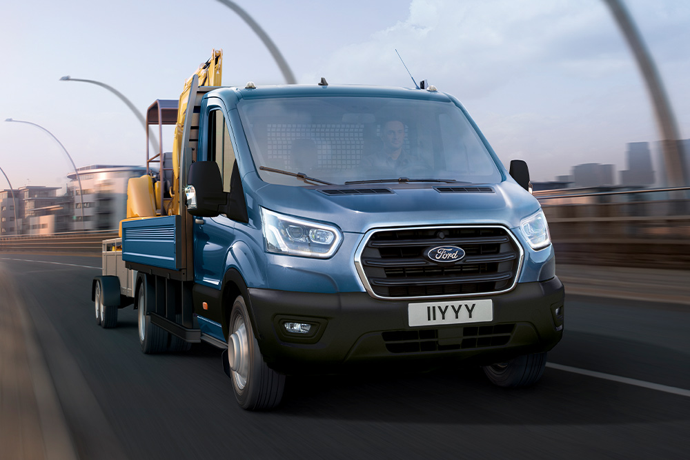 Calandre d’un Ford Transit Châssis-Cabine transportant une mini-pelle sur son plateau et circulant en milieu urbain.