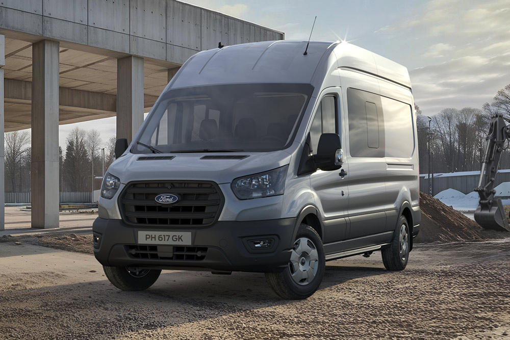 Un Ford Pro Transit argenté garé sur un chantier de construction, avec des ouvriers du bâtiment en arrière-plan.