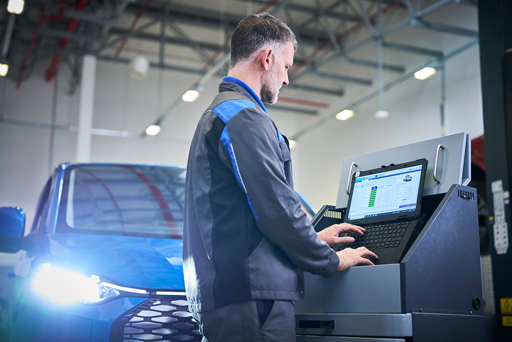Technicien travaillant sur un ordinateur portable connecté à un SUV Ford bleu dans un garage.