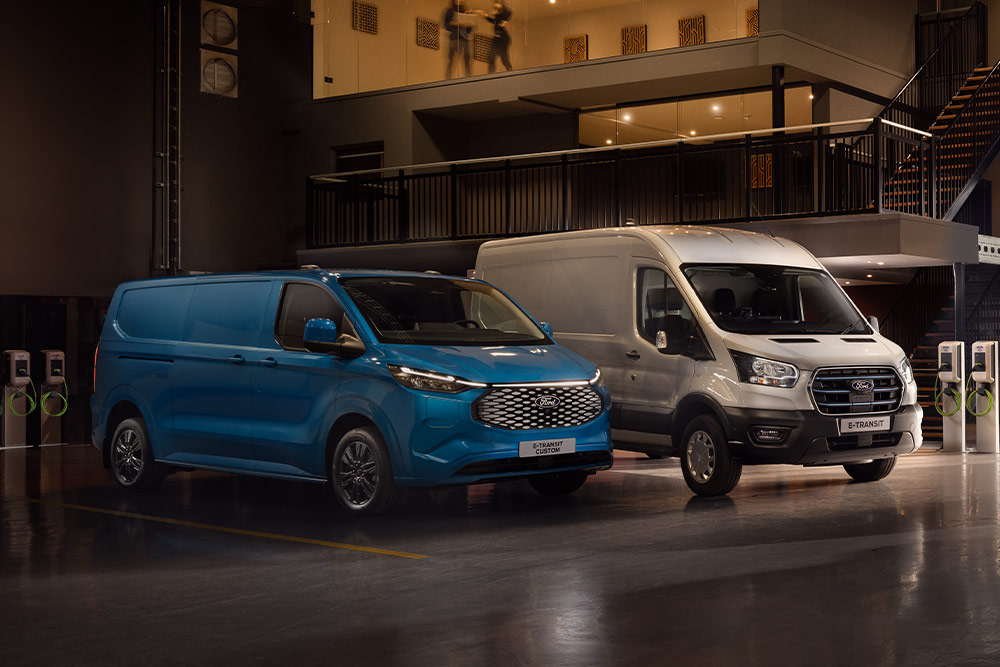 Ford E-Transit Custom bleu et Ford E-Transit argenté en cours de recharge dans un parking.