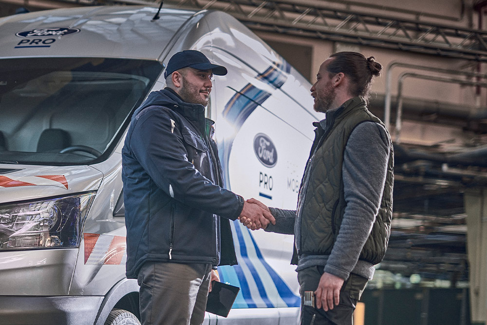 Un technicien Ford Pro discute avec un client, une camionnette Ford Pro Mobile Service est visible en arrière-plan.
