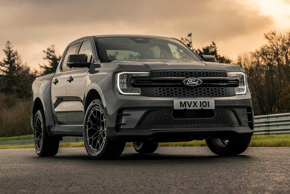 Ford Pro Ranger Plug-in Hybrid gris garé sur une route mouillée, arbres en arrière-plan.