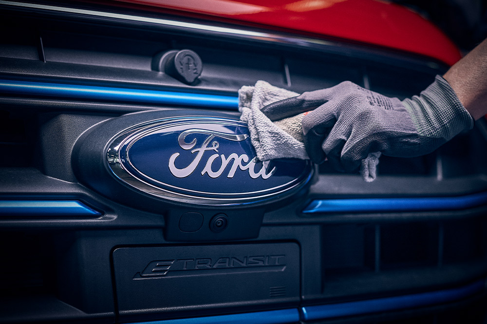 Gros plan d'un technicien polissant le logo Ford à l'avant d'une camionnette rouge.